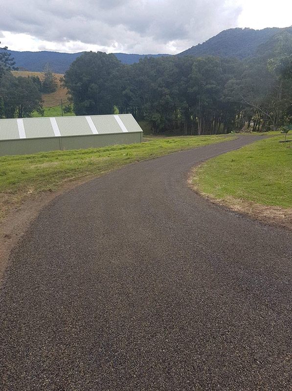 A Road Going Through a Grassy Field With a Building in the Background — North Coast Asphalts in Corindi Beach, NSW