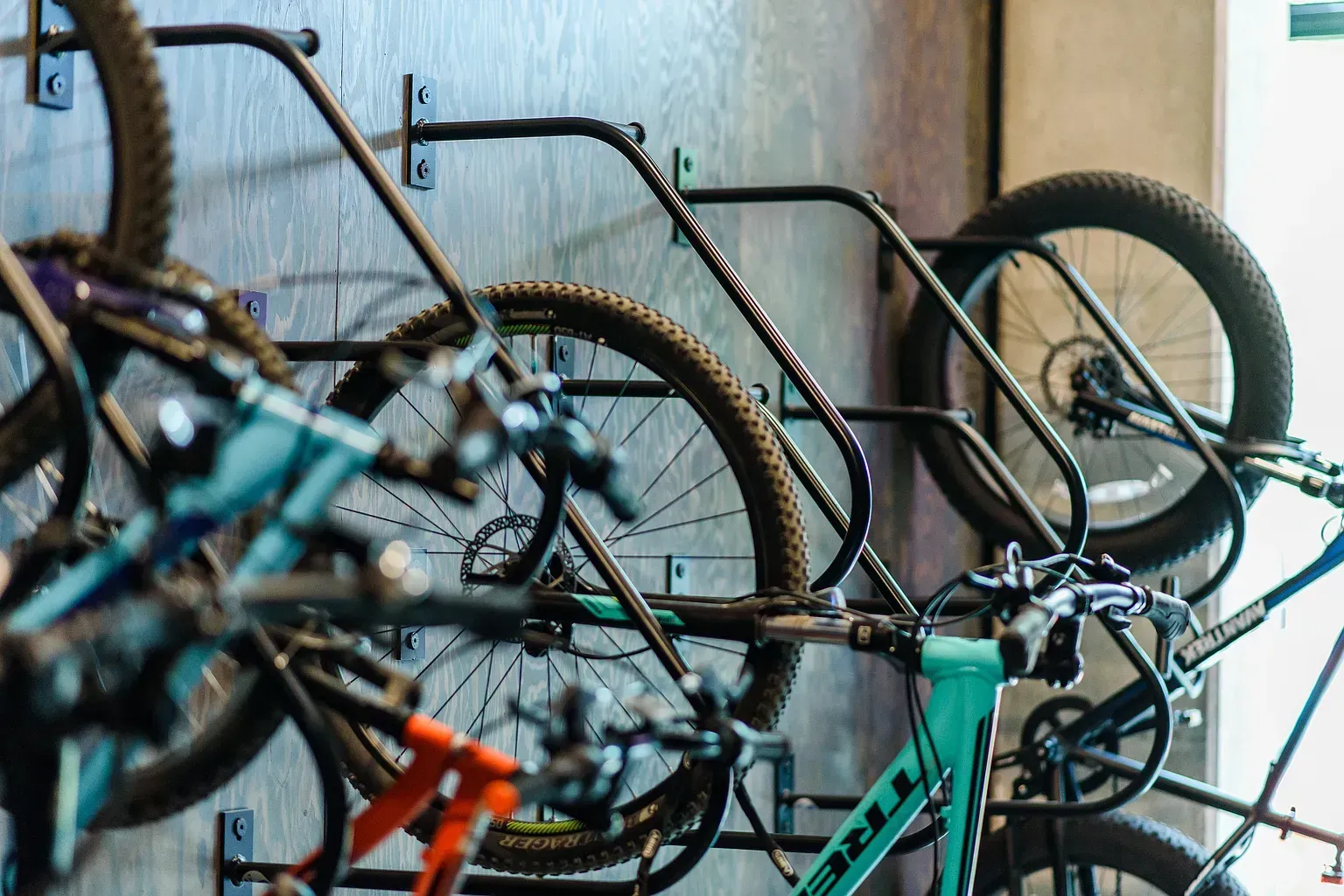 Bikes hanging on a wall-mounted rack. Various colors, partial view of wheels, handlebars.
