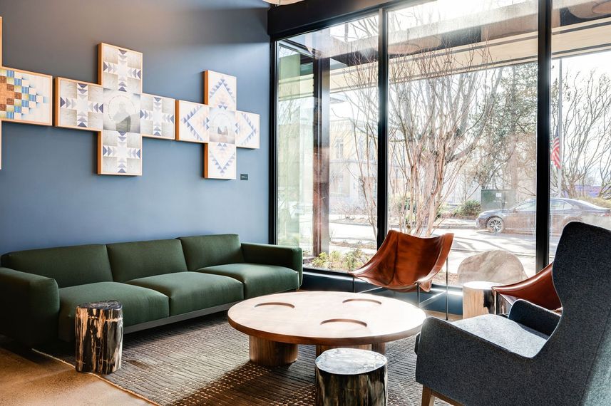 Modern lounge with green sofa, wooden table, and armchairs by a large window overlooking a garden.