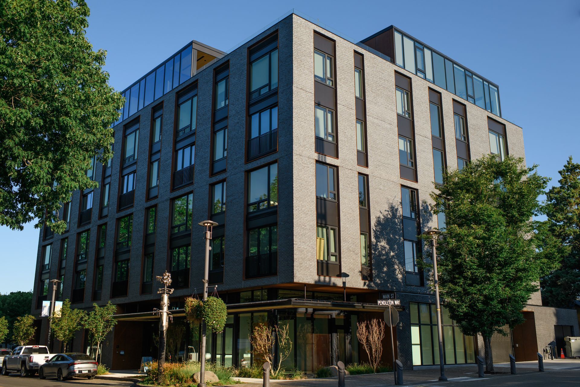 Multi-story modern building with gray brick exterior, glass windows, and ground-level retail spaces.
