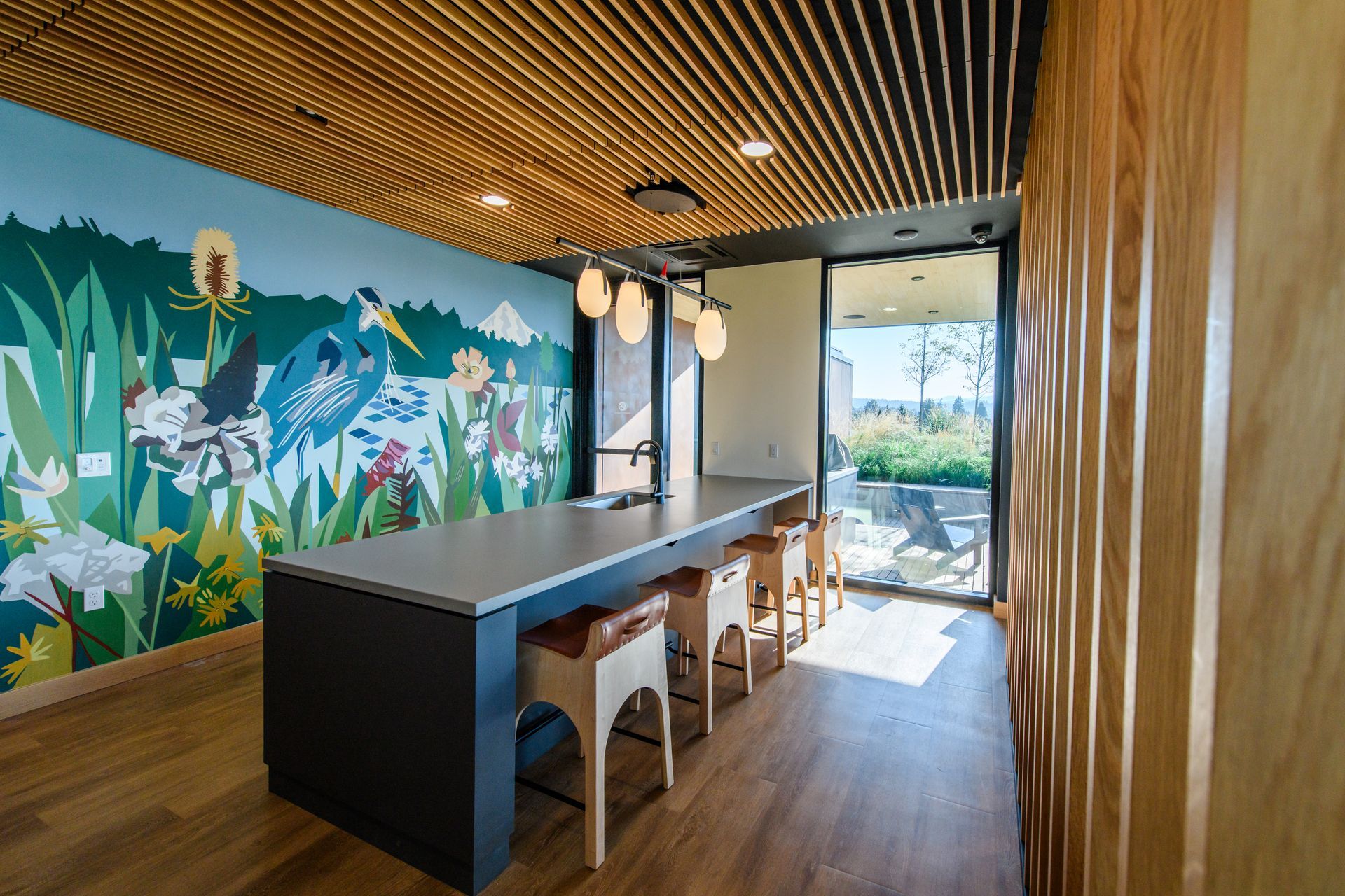 Room with mural, counter with stools, and wooden ceiling; a doorway leads outside.