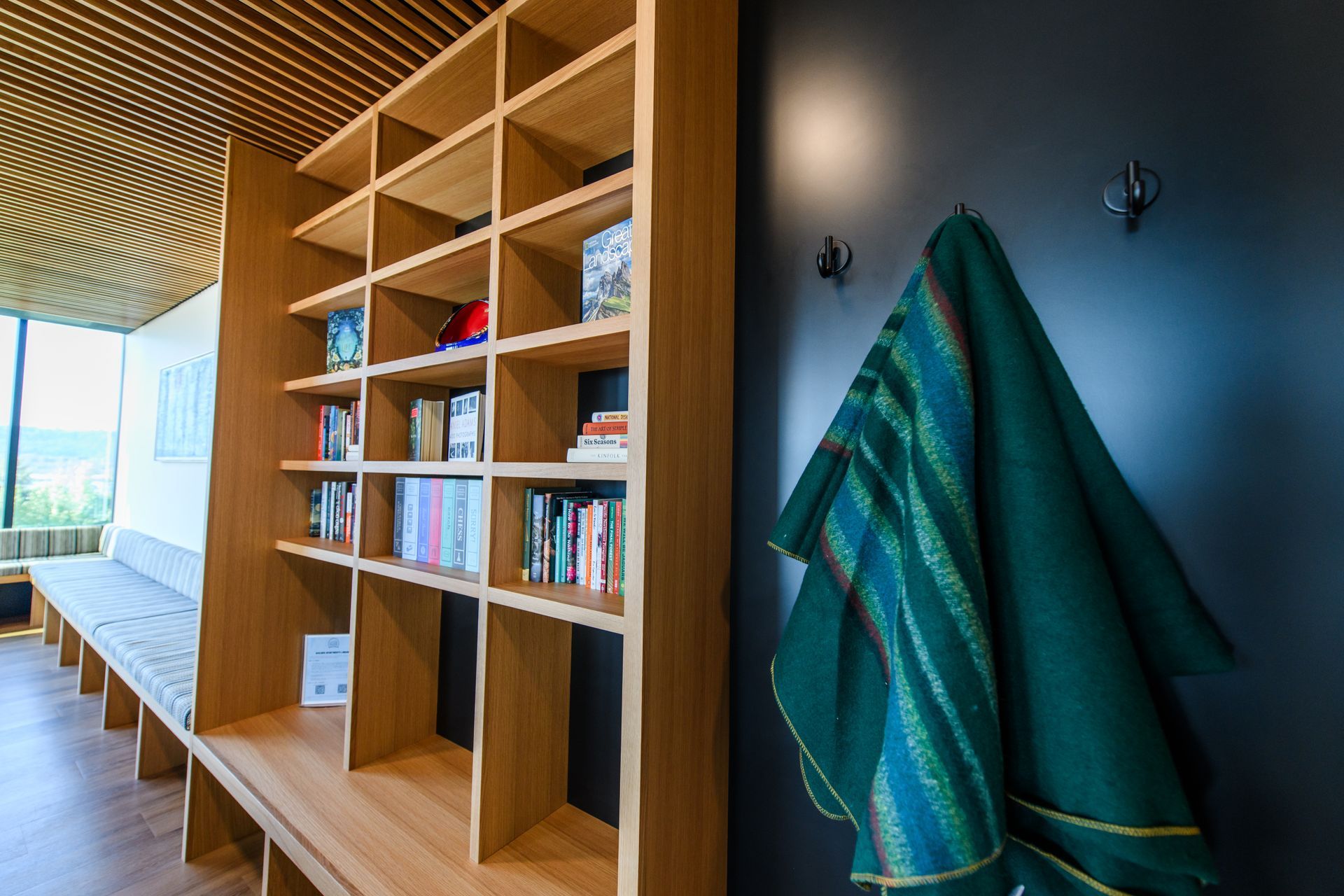 Wooden bookshelf filled with books, a bench, and a green coat on a black wall.