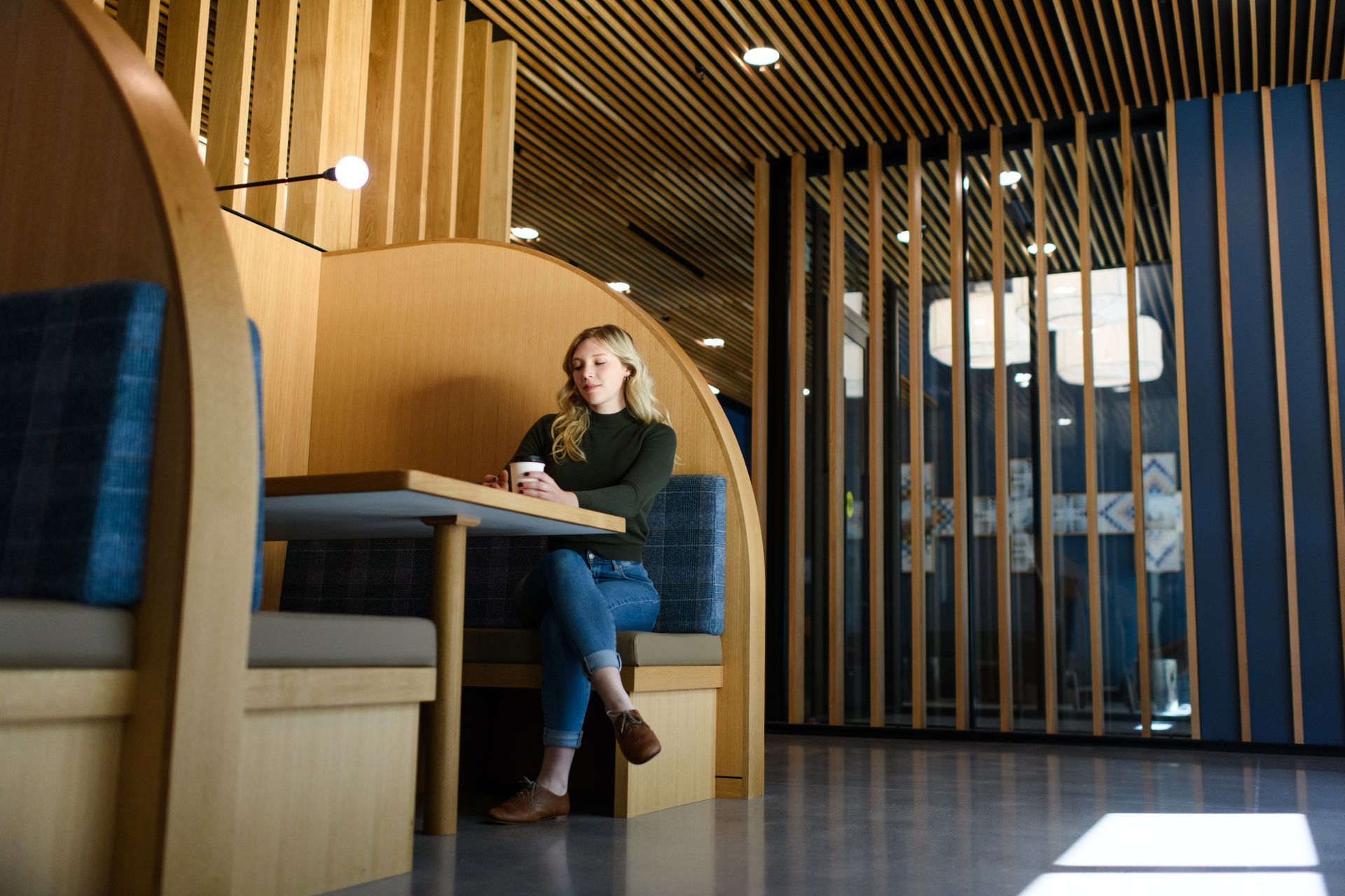 Woman sitting at a table in a booth, in a modern, wood-paneled space.