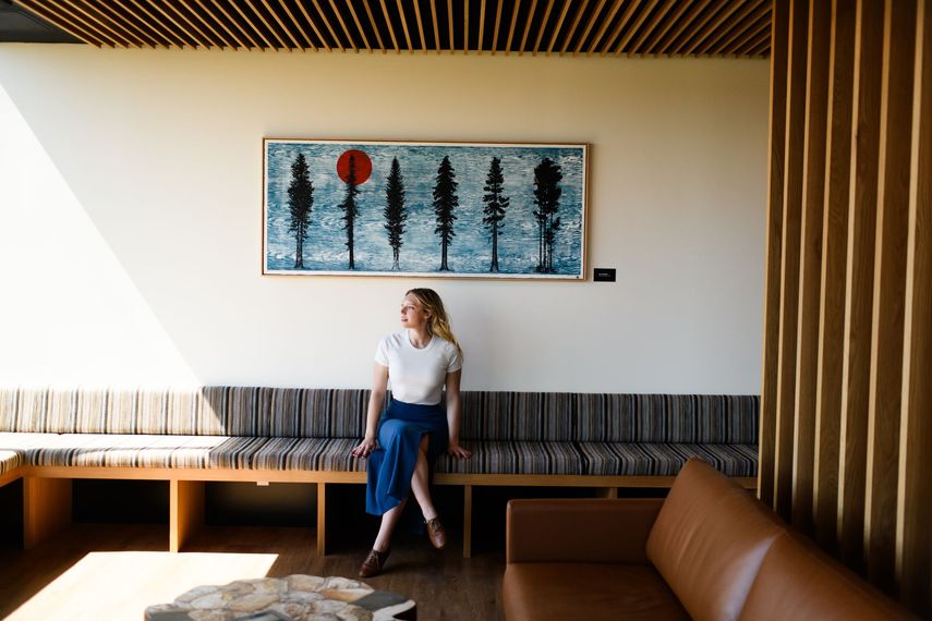 Woman sitting on a bench, looking to the side, in a room with artwork and wood accents.