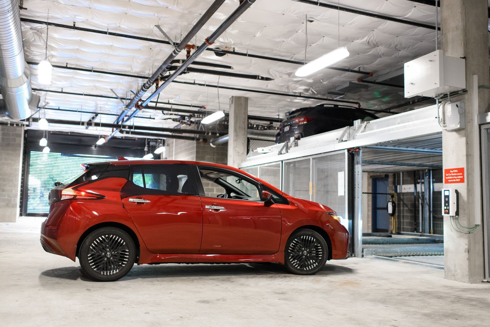 Red car inside a parking garage with mechanical lift and structural columns.