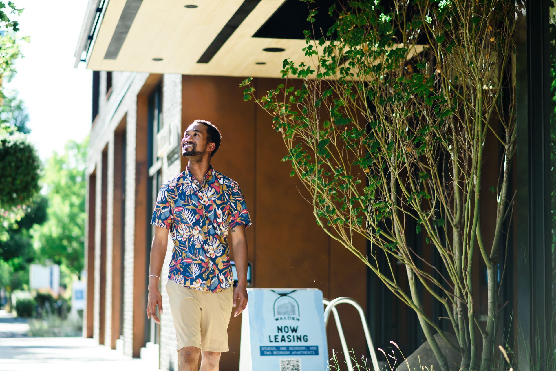 Man in floral shirt, tan shorts walks under awning past 