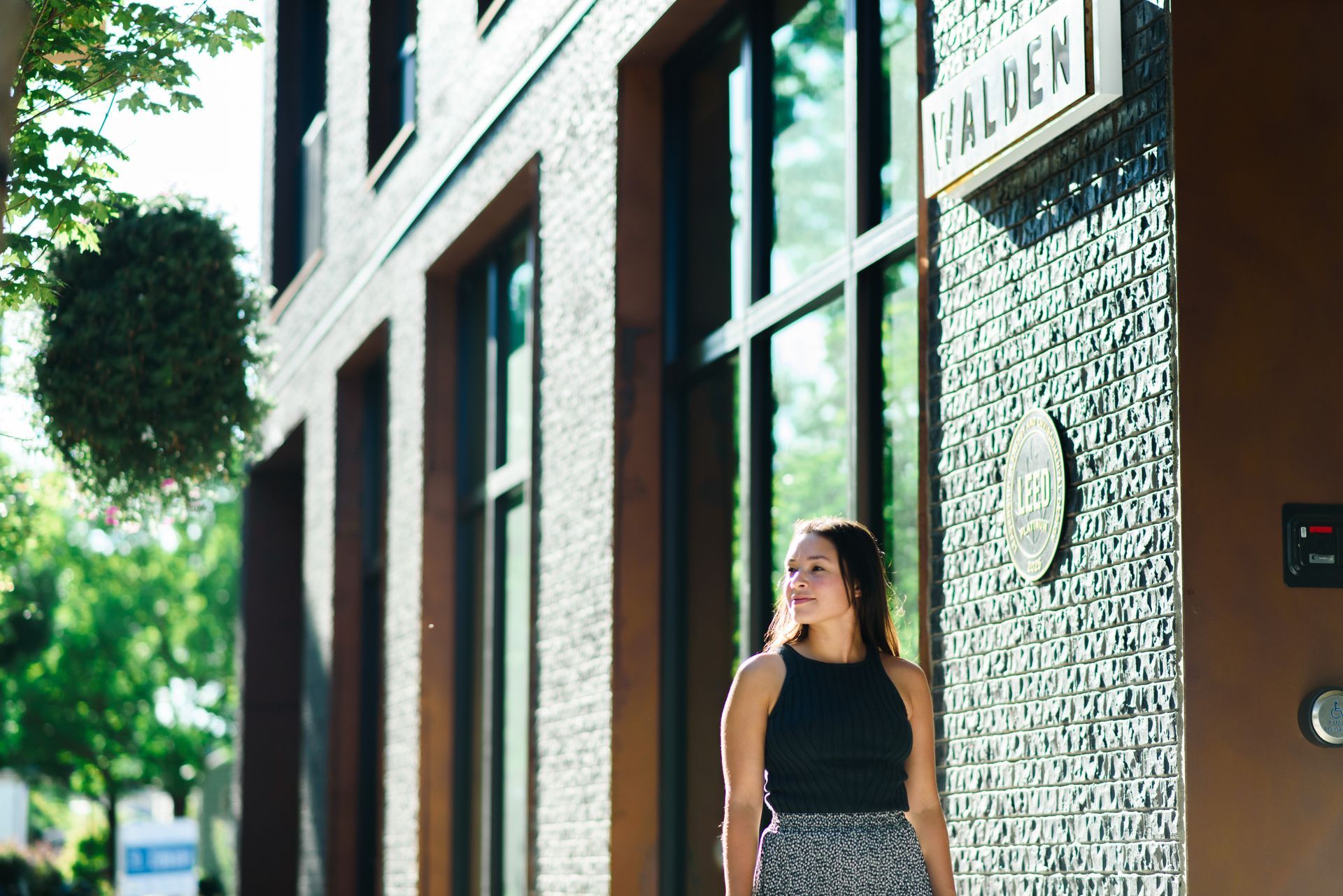Woman walks past the Halden sign on a building with textured brown brick, green plants.