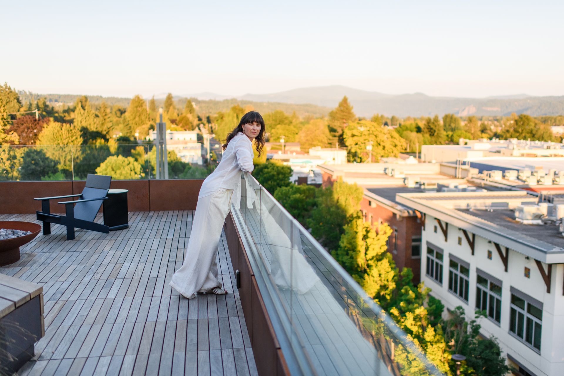 Woman leaning on a railing, smiling, with a city and mountain view in the background.
