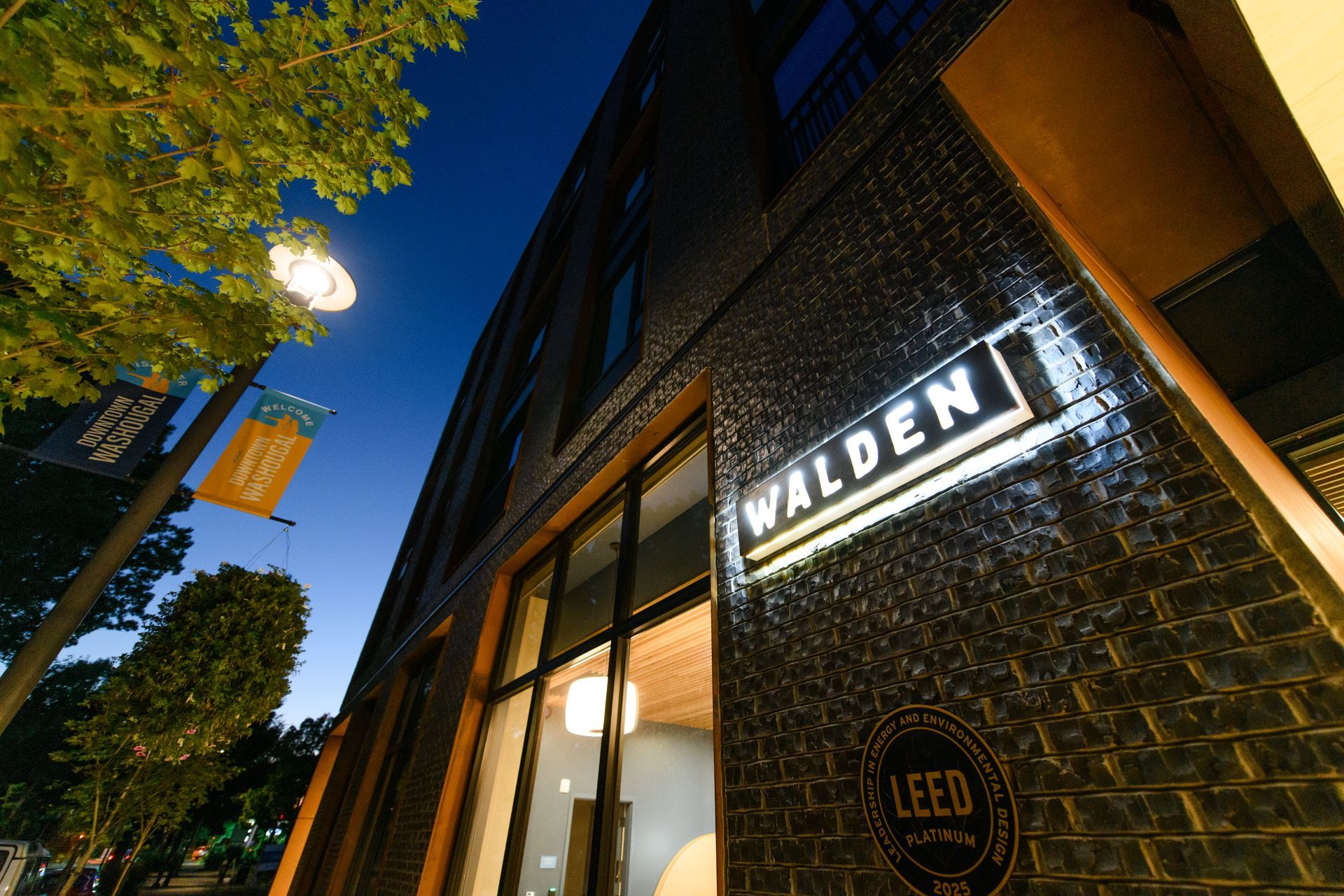 Walden building at dusk with illuminated sign, brick exterior, and LEEDS logo.