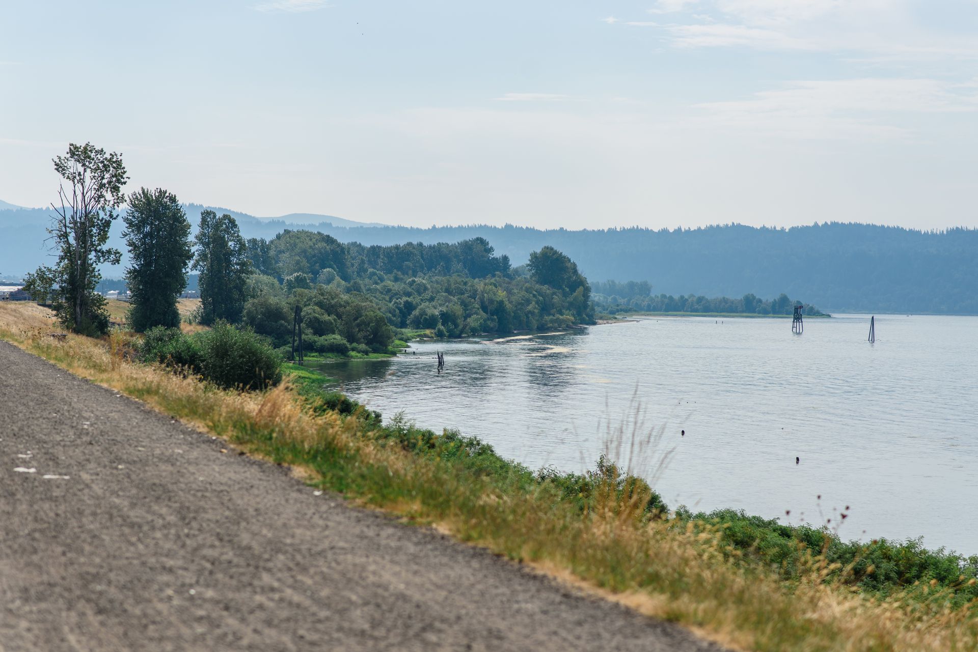 Lakeside view with trees on the shore, a paved road in the foreground, and hazy mountains in the distance.