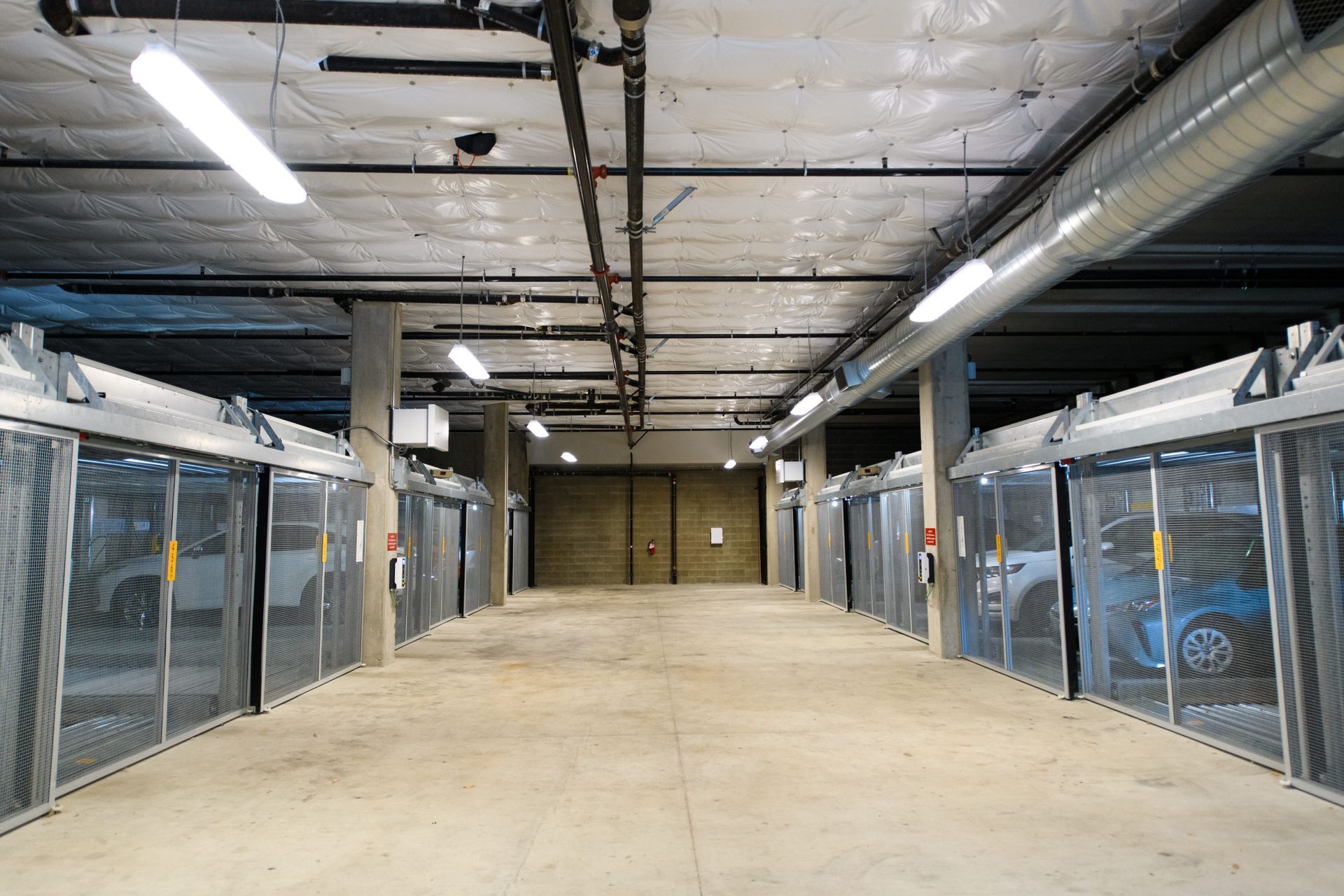 Underground parking garage with rows of gated storage units and overhead lighting.