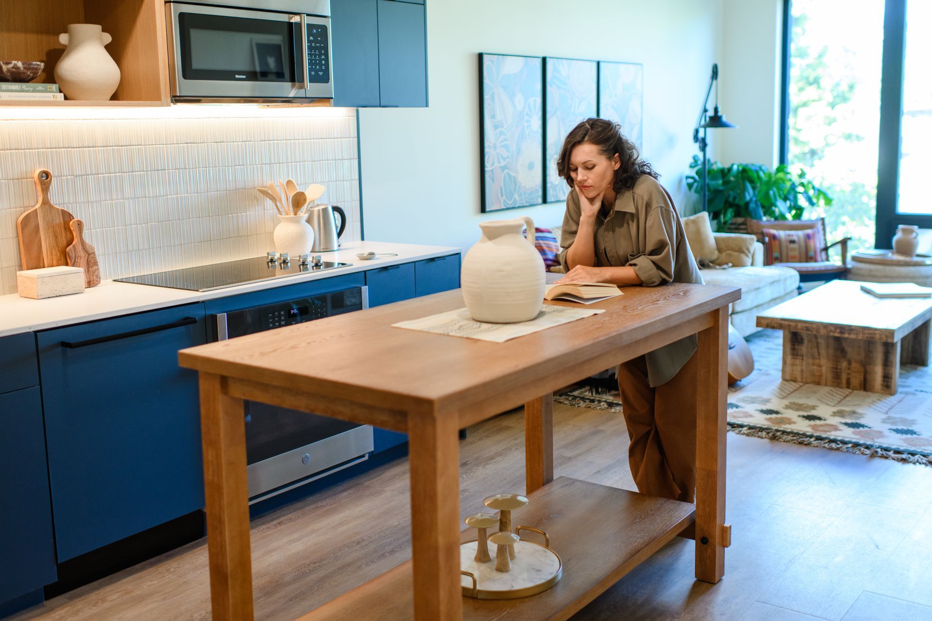 Woman reading at a kitchen island in a modern apartment, natural wood tones and blue cabinets.