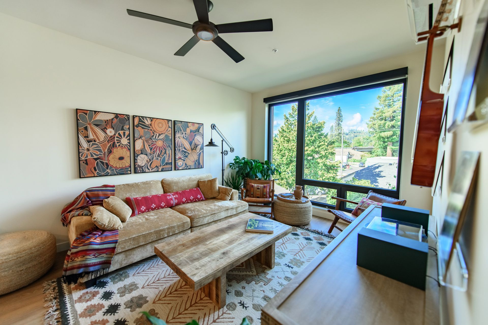 Cozy living room with large window, sofa, wooden coffee table, and art on the wall.