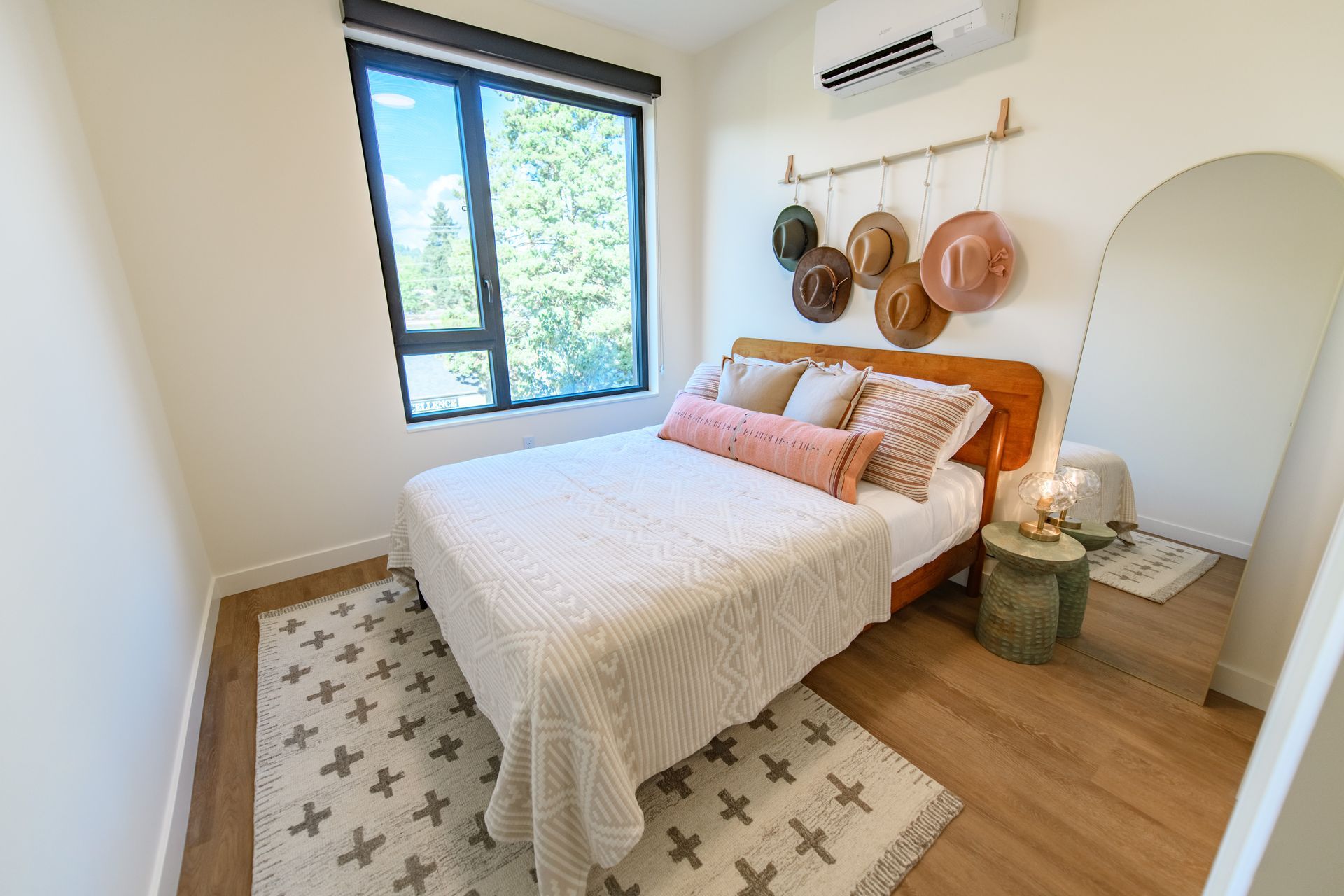 Cozy bedroom with bed, rug, window, and mirror; hats hang above the bed.
