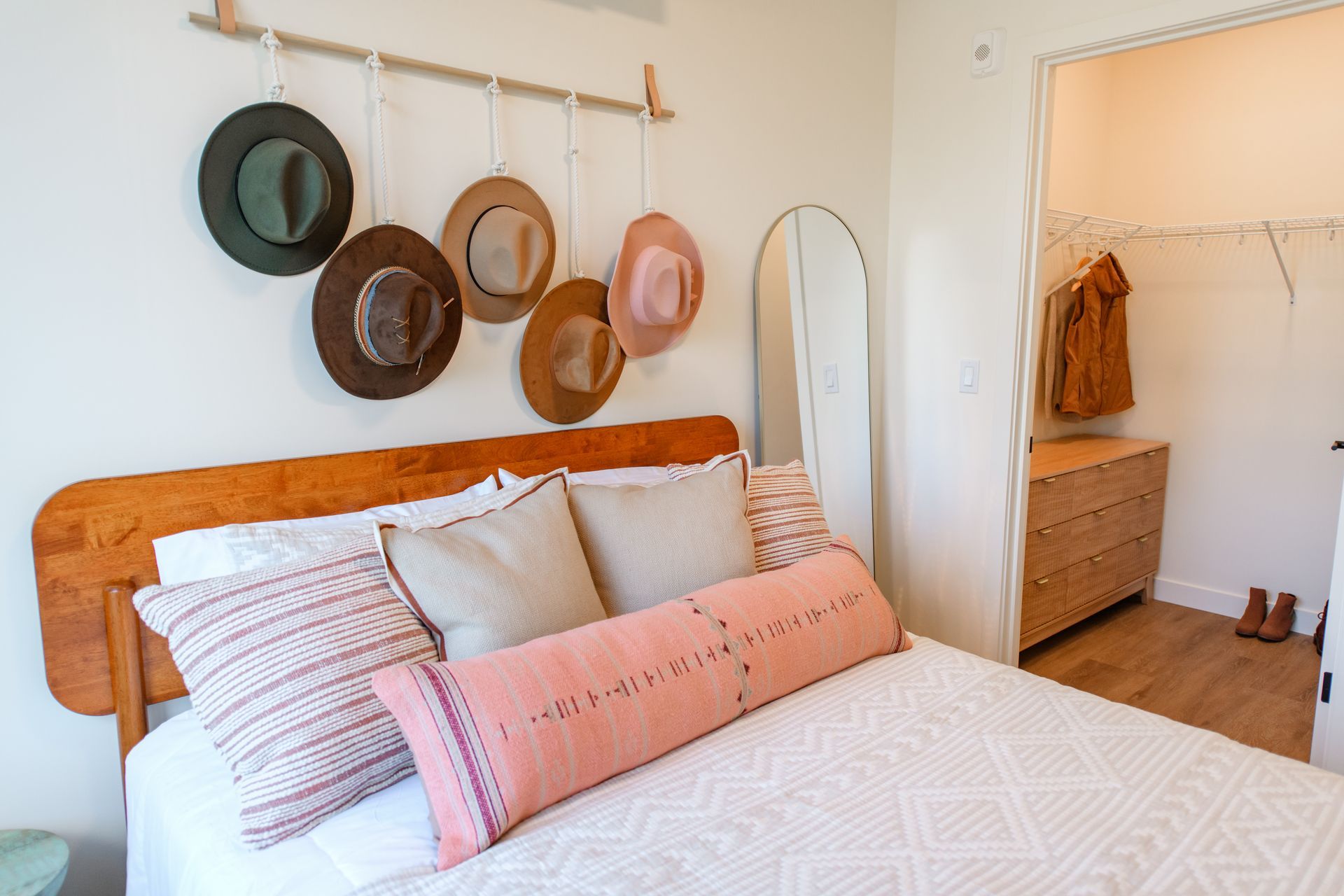 Bedroom with bed, hats hanging on the wall, and a closet. Beige, pink, and brown color scheme.
