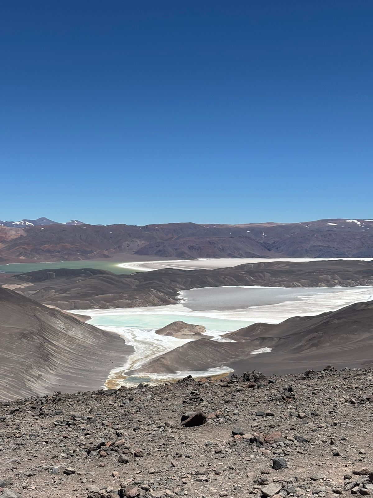 Un vasto paisaje de gran altitud con lagos turquesas y blancos, rodeado de oscuras rocas volcánicas y montañas