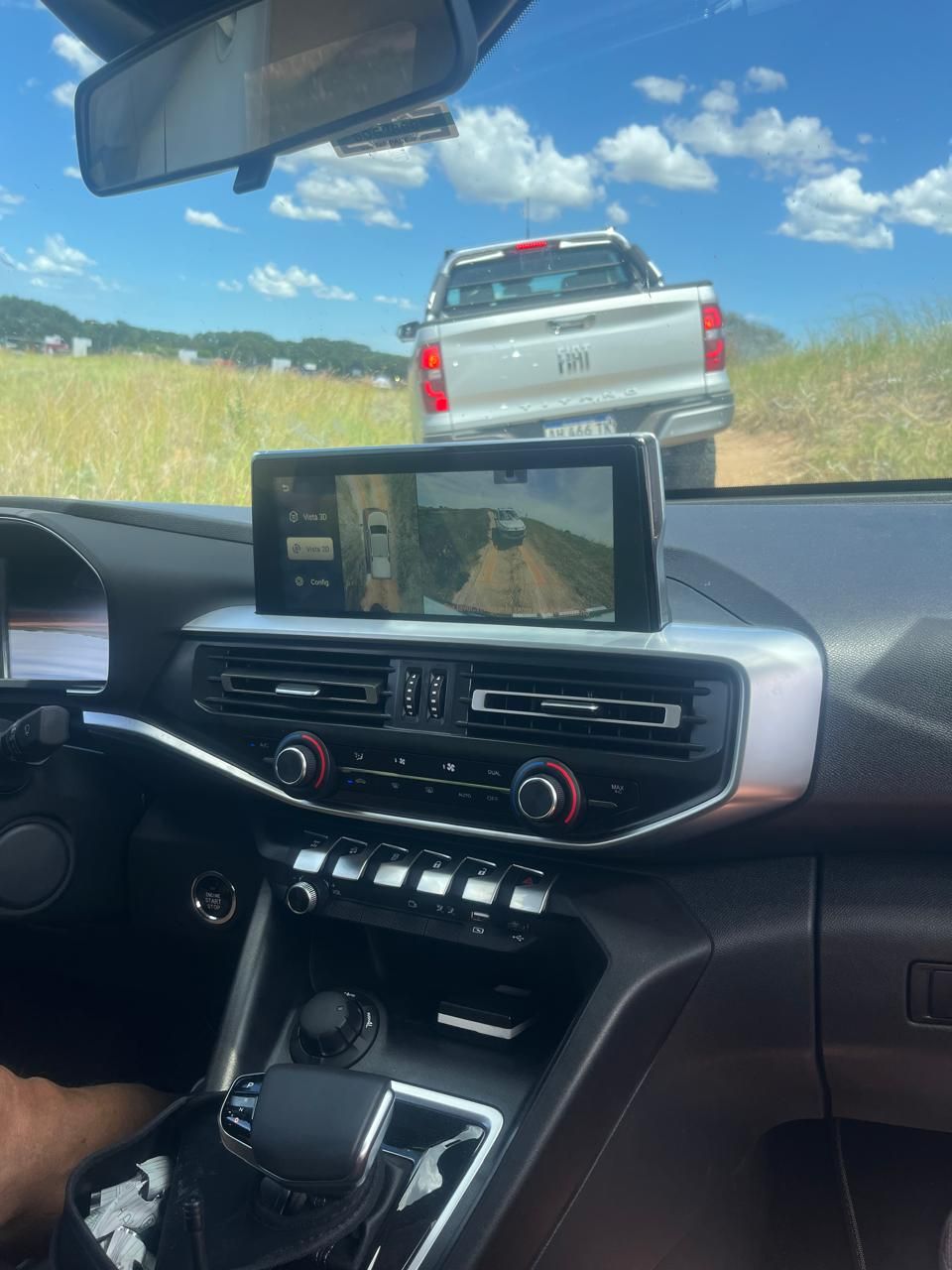 Fotografía del interior del coche, con el tablero, y una camioneta delante, en un camino de tierra. Día soleado.