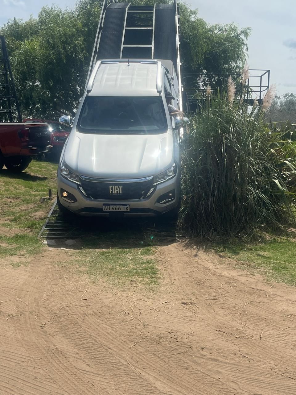 Camioneta plateada en una rampa, lista para subir. Al aire libre, día soleado.