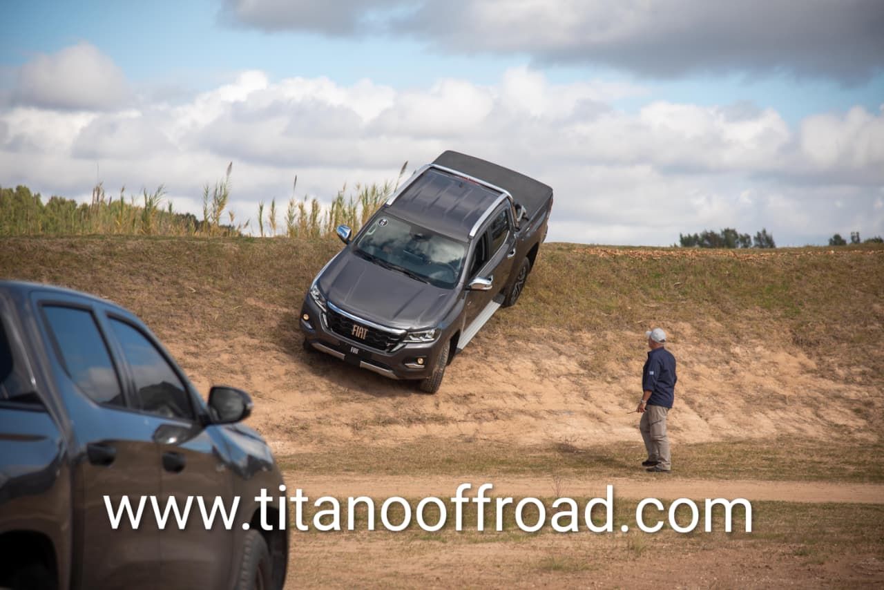 Un SUV negro inclinado sobre un terraplén de tierra, con un hombre de pie cerca y otro vehículo a la izquierda.