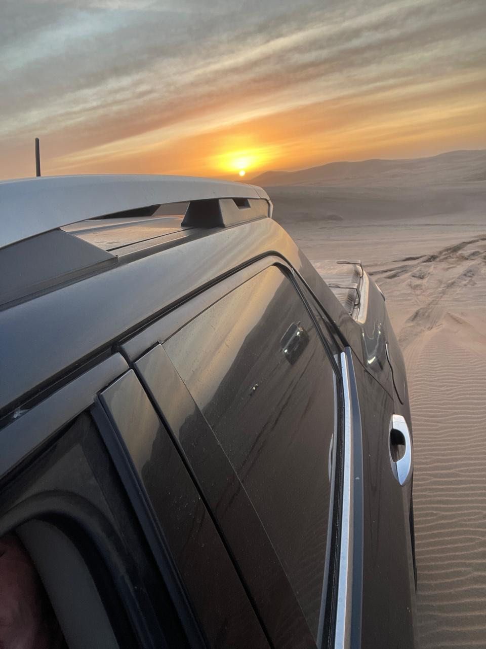 SUV en una duna de arena con puesta de sol de fondo.