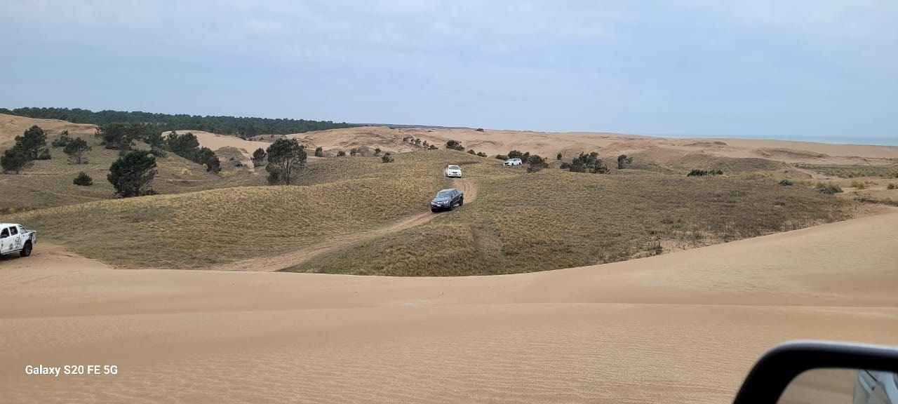 Un vehículo circula por un paisaje arenoso y lleno de dunas bajo un cielo nublado.
