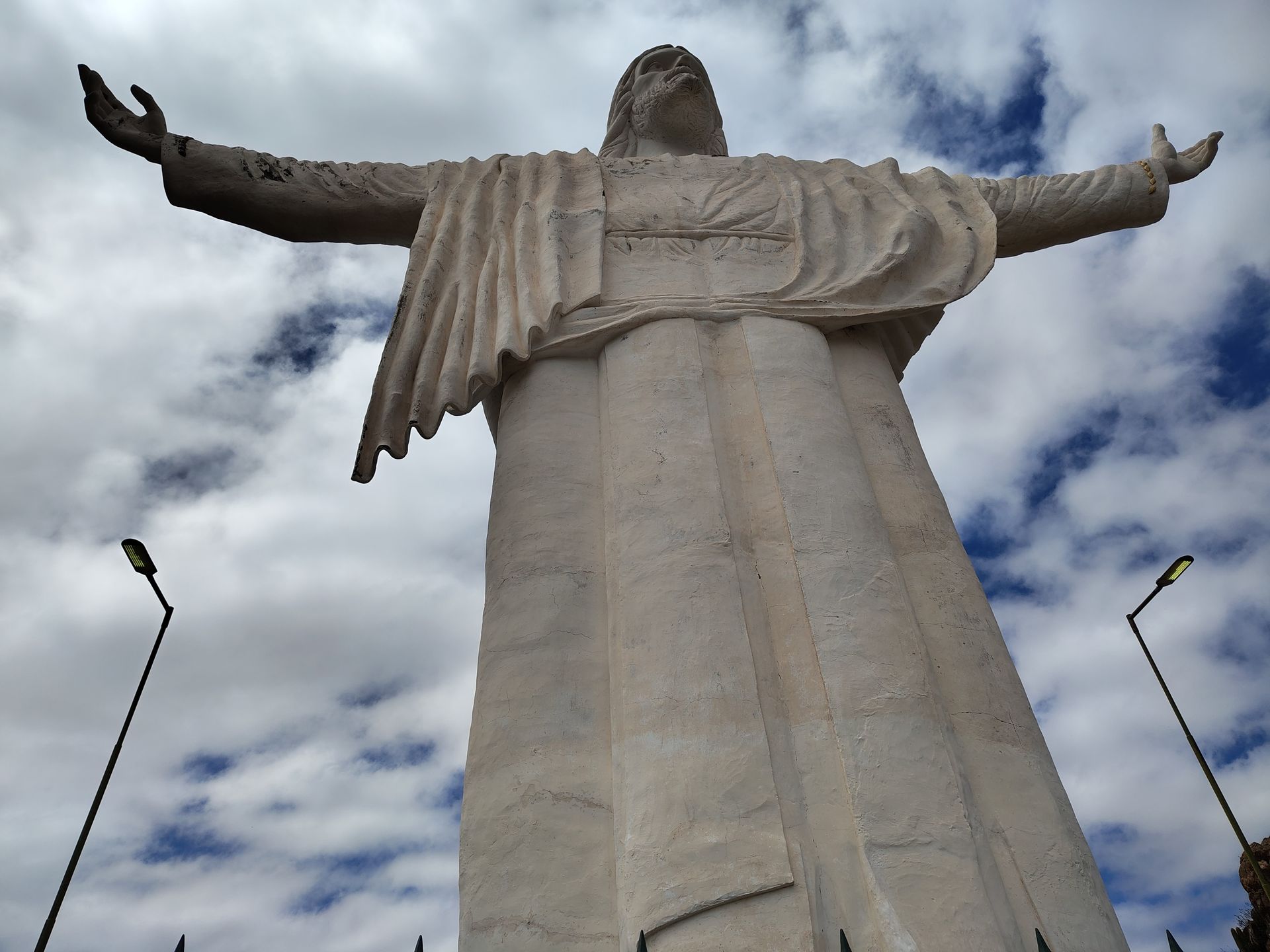 Una gran estatua de Cristo de color claro con los brazos extendidos, contra un cielo azul nublado.