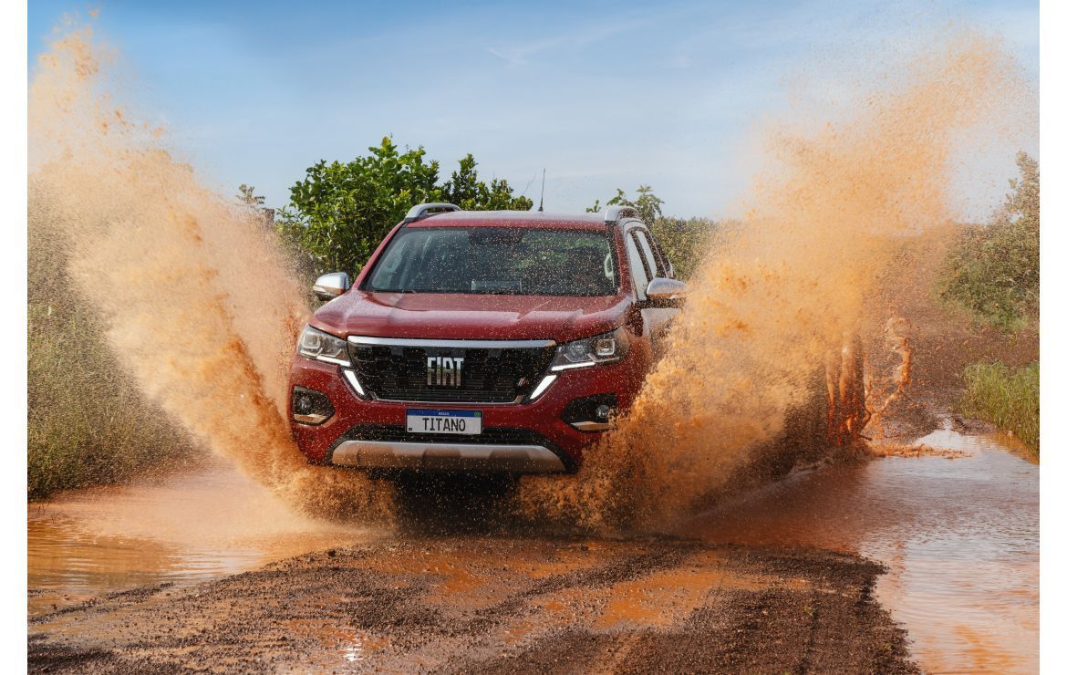 Camioneta Fiat roja chapoteando en agua fangosa en un camino de tierra.