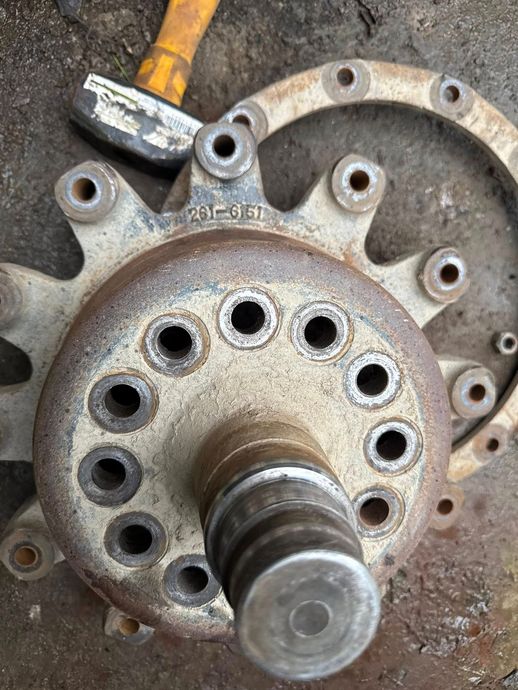 Rusty metal hub with multiple holes, shaft, and flange, with hammer visible.