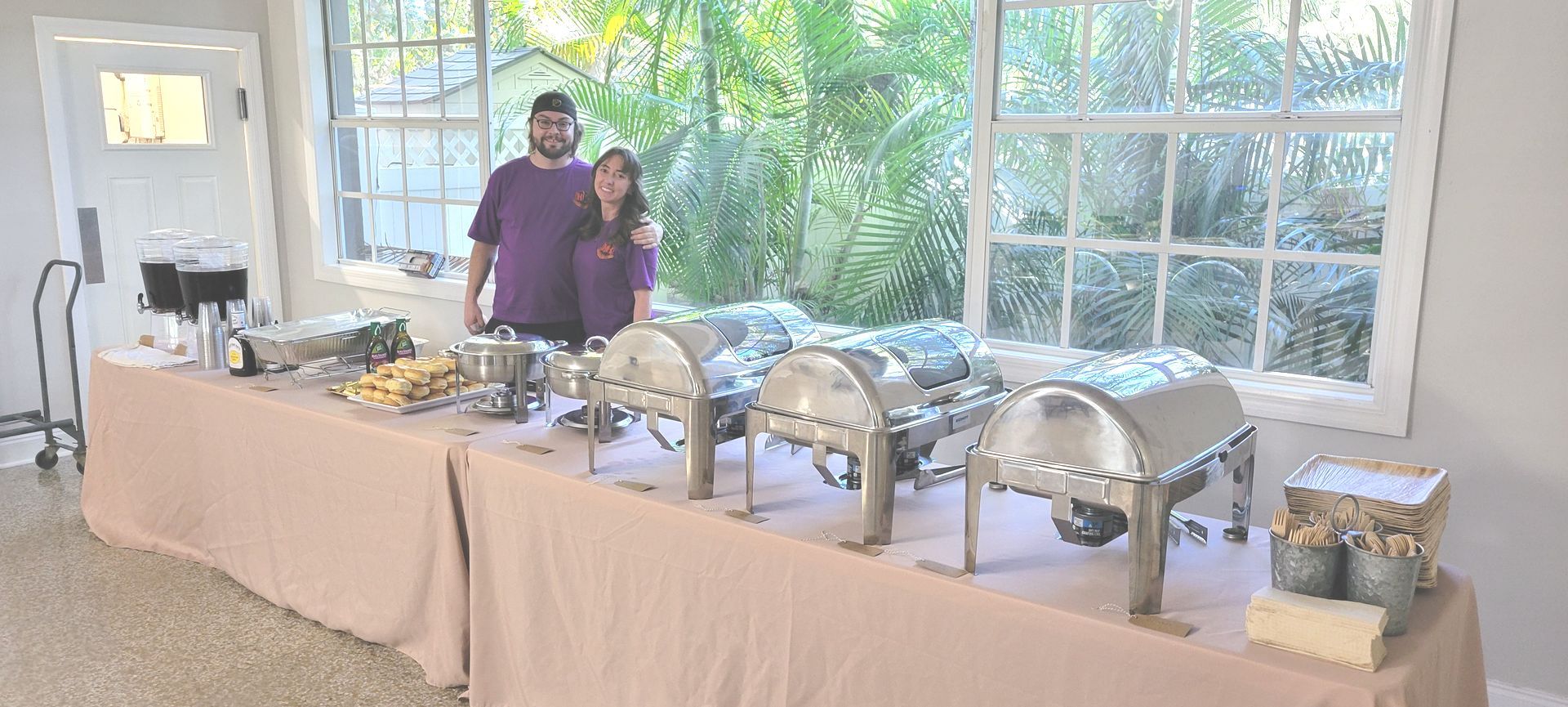 A man and a woman are standing in front of a long buffet table.