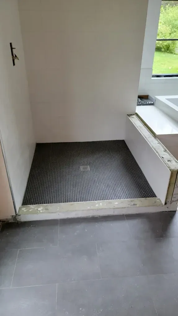 A residential shower stall under construction with a dark-tiled floor and unfinished white walls in a modern bathroom.
