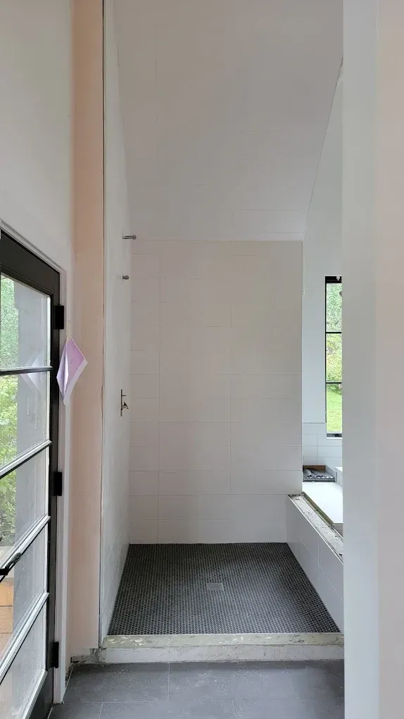 A view looking into a shower with patterned dark tiles and light walls, adjacent to a glass-paneled door.