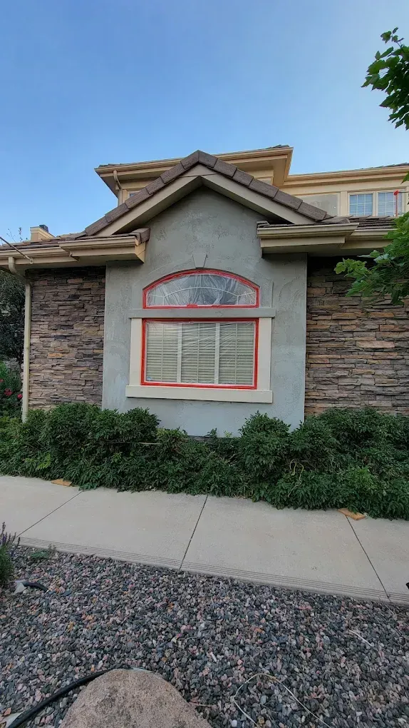 A single-story home exterior featuring a stone-clad facade, stucco accent wall, and a large arched window with red trim.