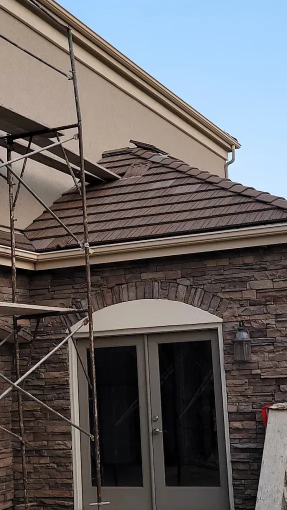 Scaffolding set up against a stone building with a tiled roof near a double-door entryway.