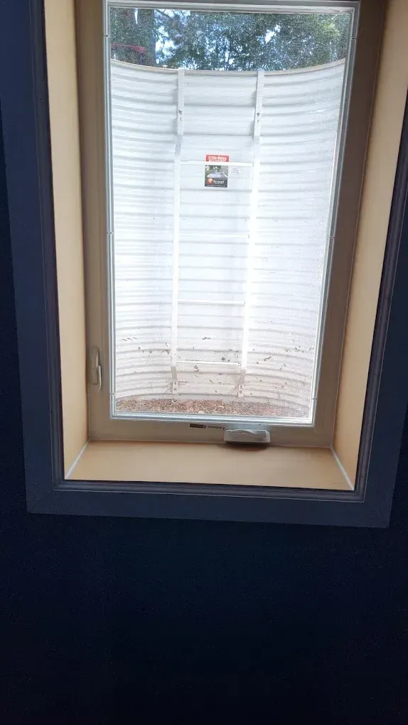 A white egress window well visible through a basement window, framed by beige walls and dark trim.