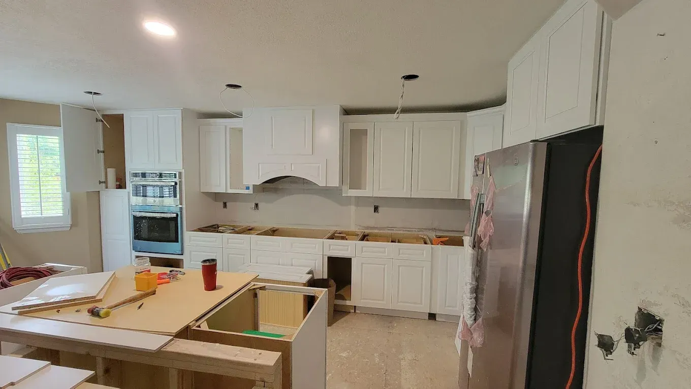 A kitchen under renovation with white cabinets, a large stainless steel refrigerator, and unfinished island countertops.