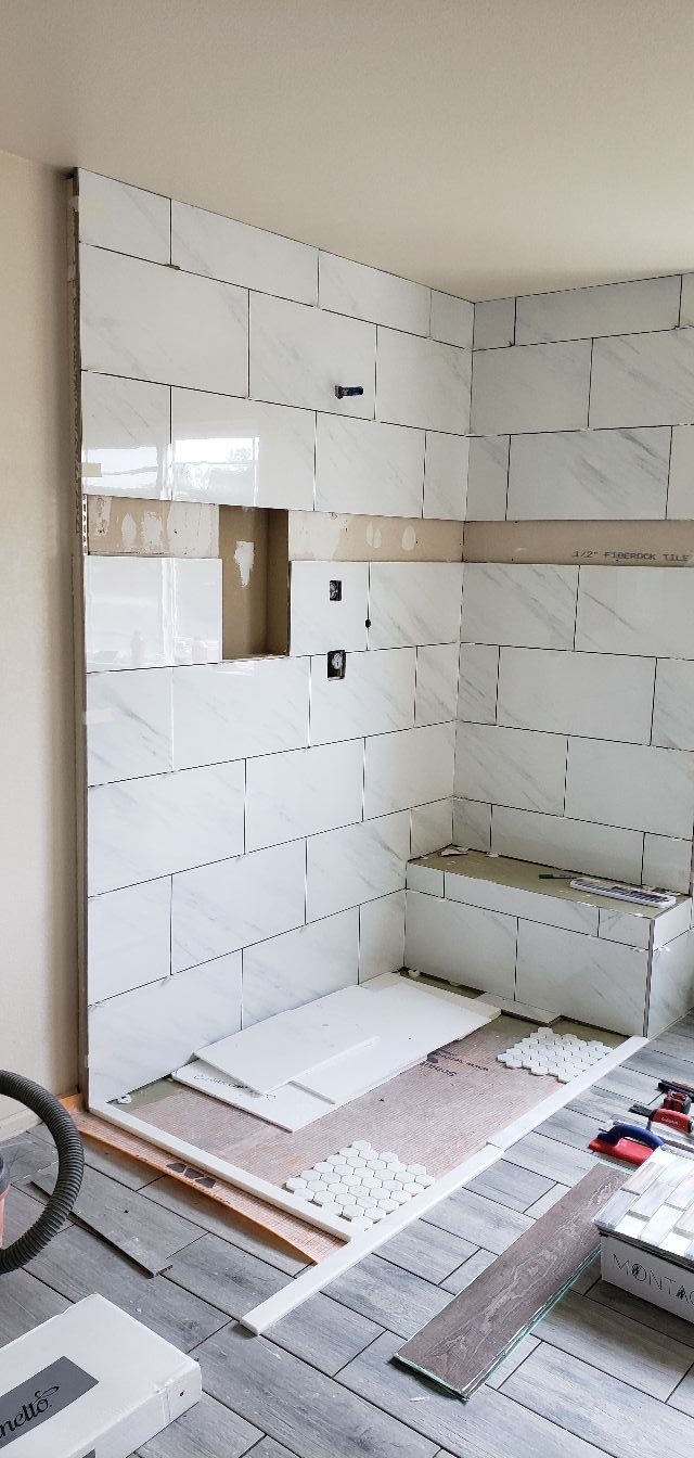 A partially tiled shower enclosure with large white marble-look tiles, a built-in niche, and a tiled bench seat.