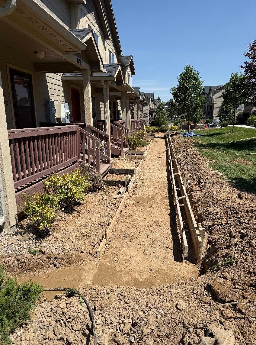 A row of townhomes with a dirt trench and wooden concrete forms prepared for a new walkway along the front porches.