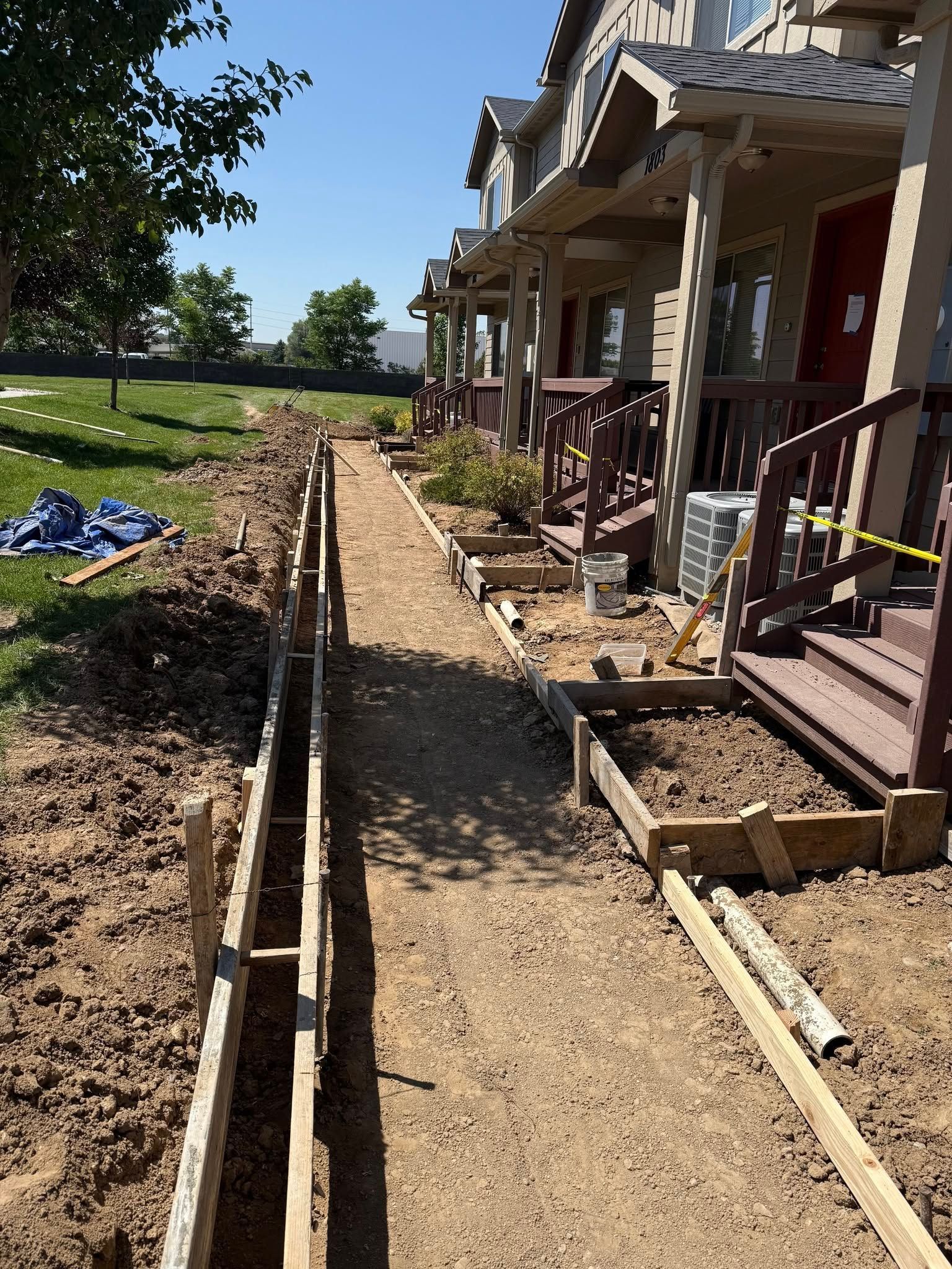 A construction site showing wooden forms installed for a new sidewalk alongside a row of townhouses.