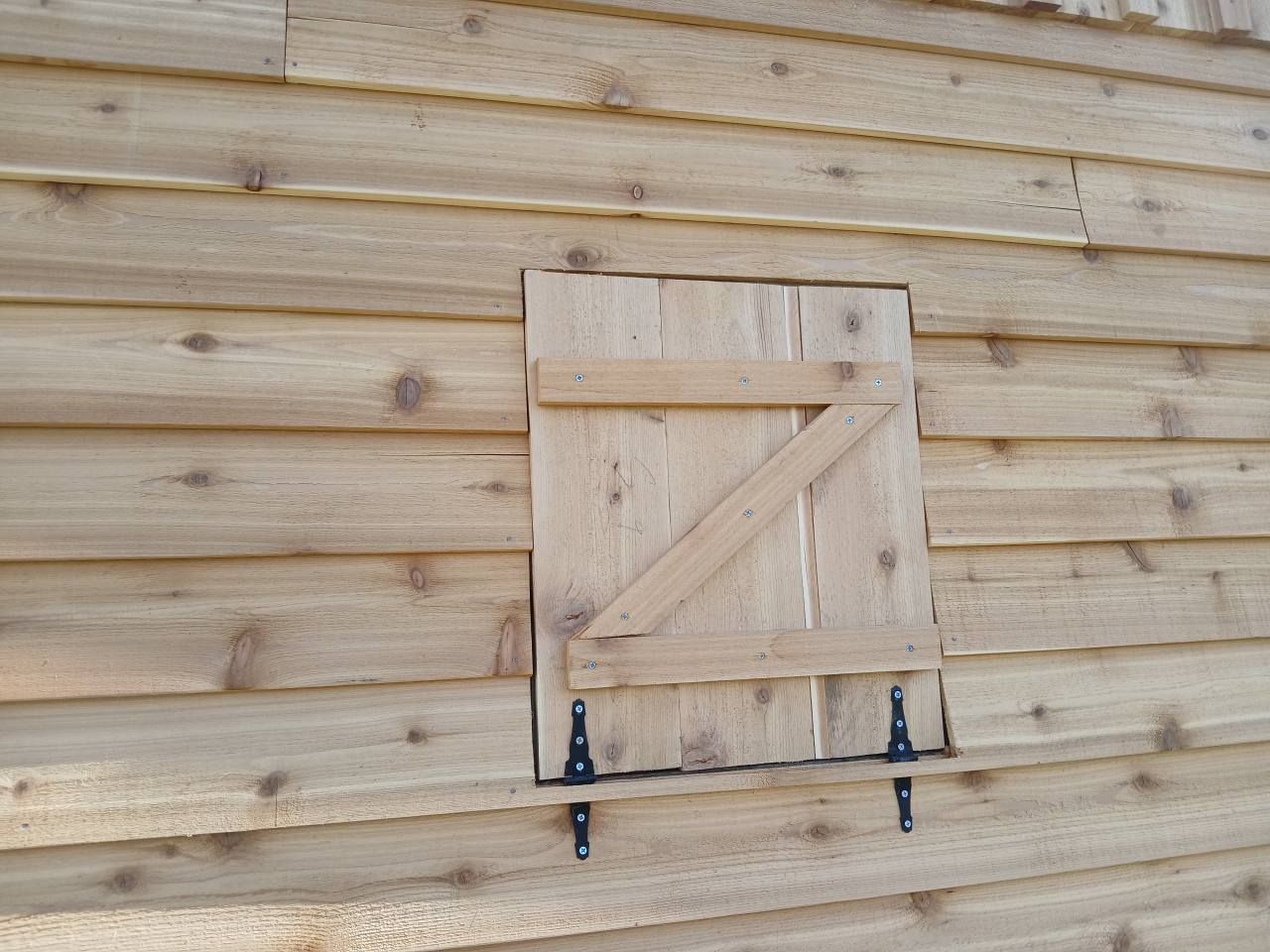 A light-wood barn wall featuring a hinged, rectangular wooden access door with a Z-shaped support brace.