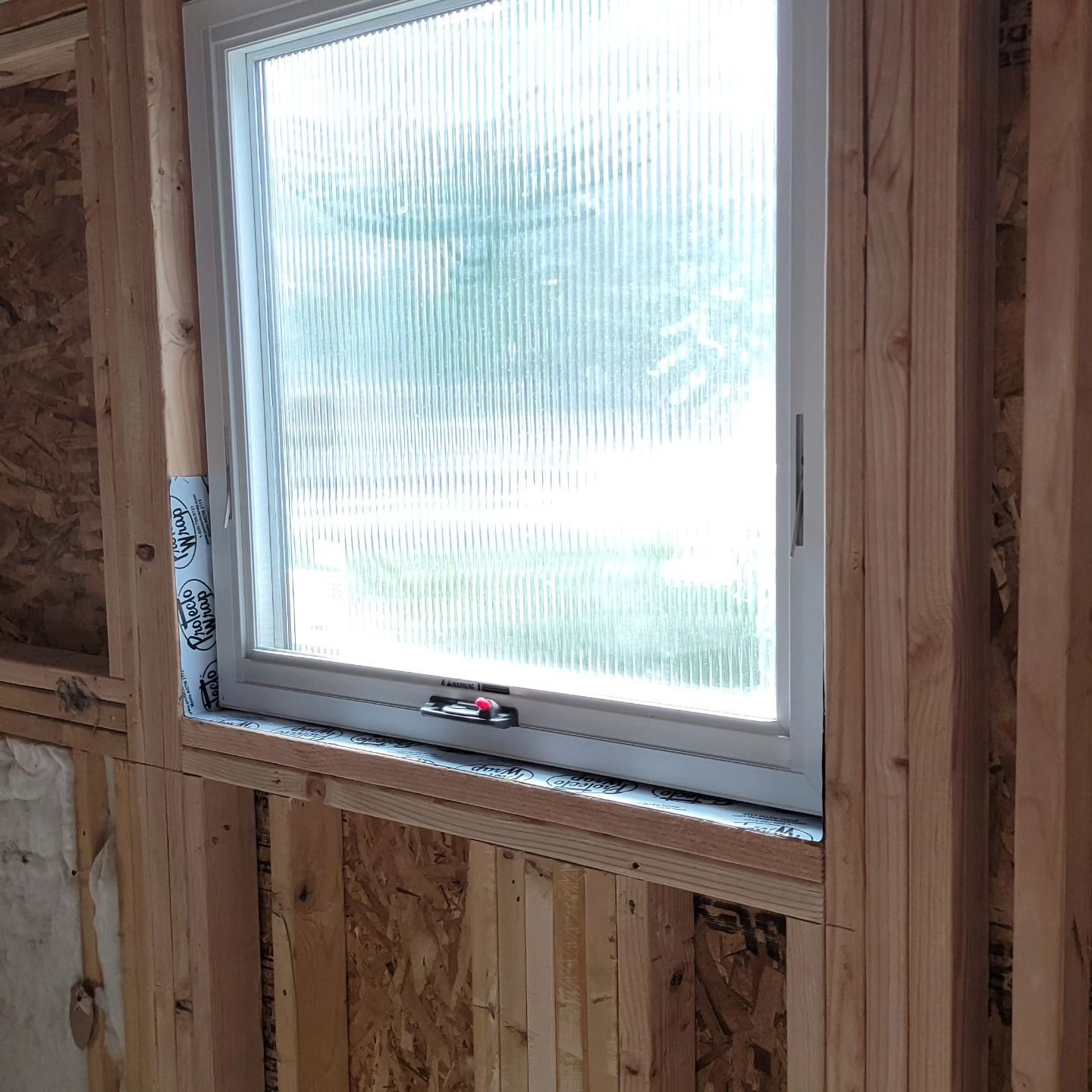 An installed rectangular window with patterned privacy glass set within a wooden interior wall frame.