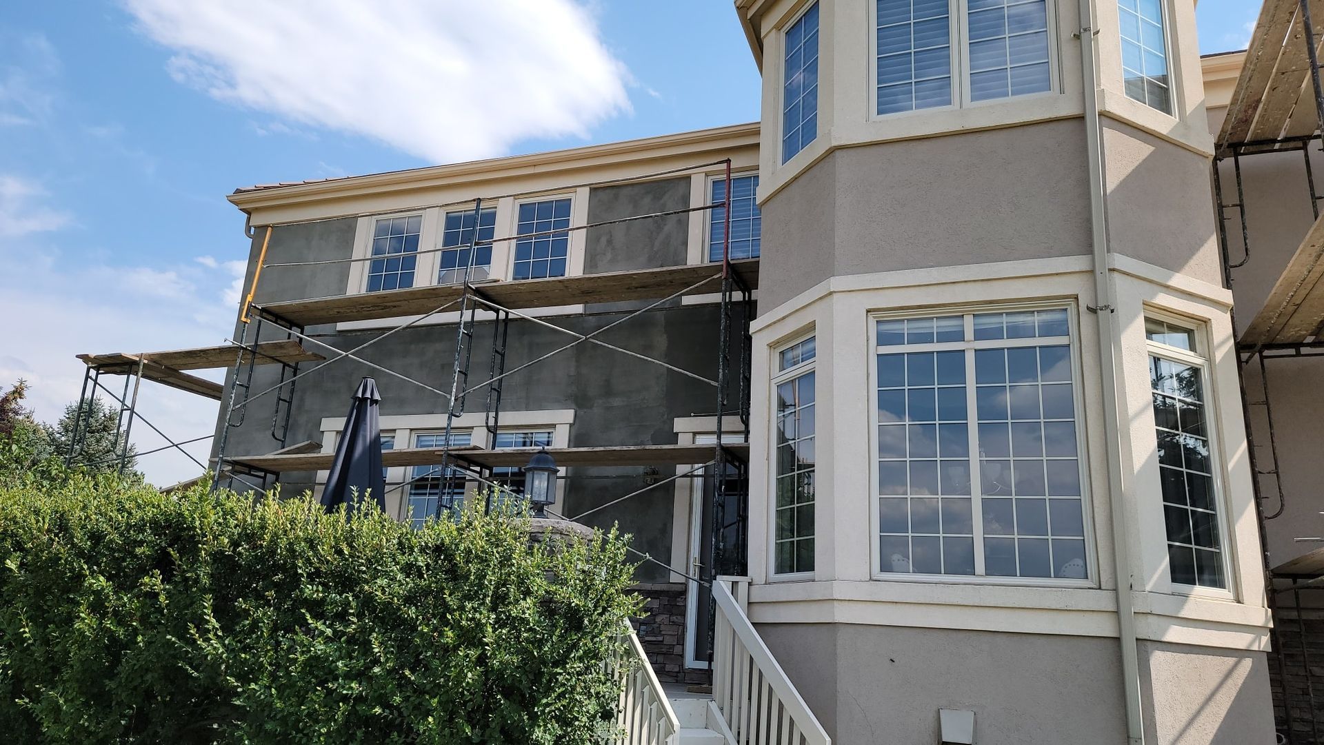 A multi-story beige house under renovation with scaffolding set up in front of the walls and windows.