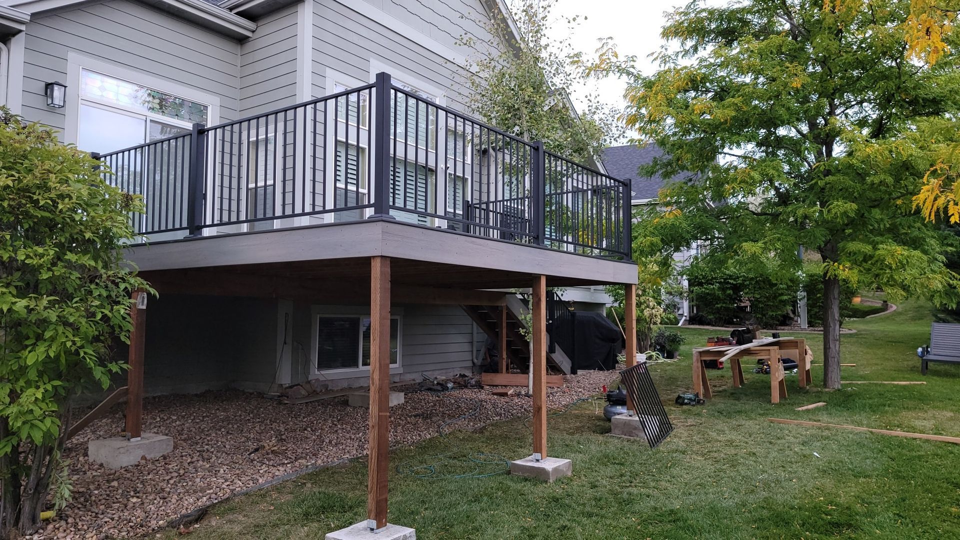 A raised wooden deck with a black metal railing extends from a light-colored house over a gravel-covered backyard.