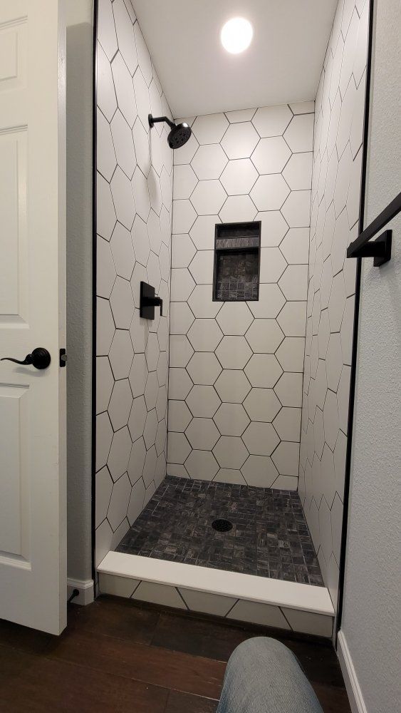 A small walk-in shower with white hexagonal tiles, a dark stone floor, and matte black fixtures.