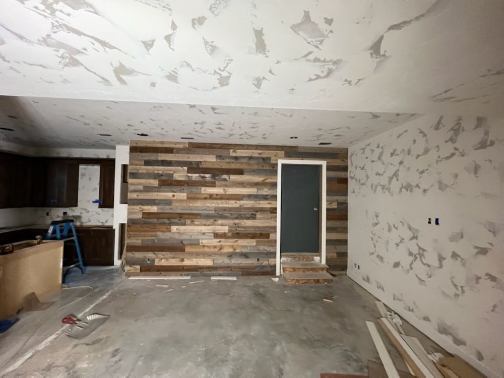 An unfinished room featuring a rustic reclaimed wood accent wall, partially painted walls, and a kitchen area.