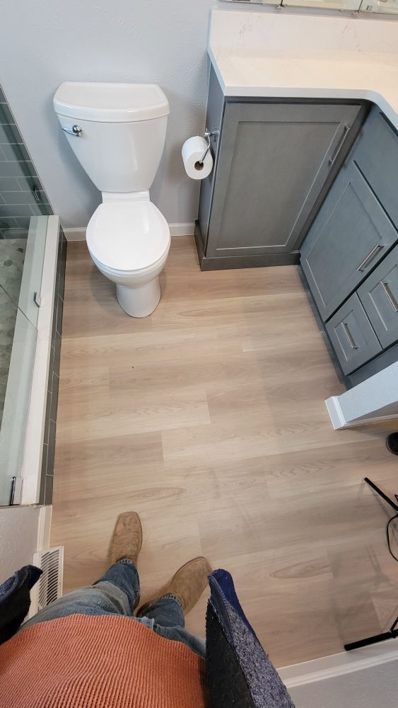 A first-person view of a bathroom with light wood-look flooring, a white toilet, and a grey vanity cabinet.