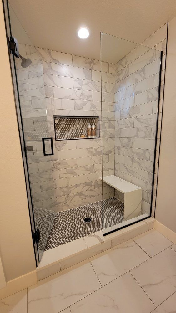 Modern walk-in shower with white marble-look wall tiles, a black patterned floor, a glass door, and a built-in seat.