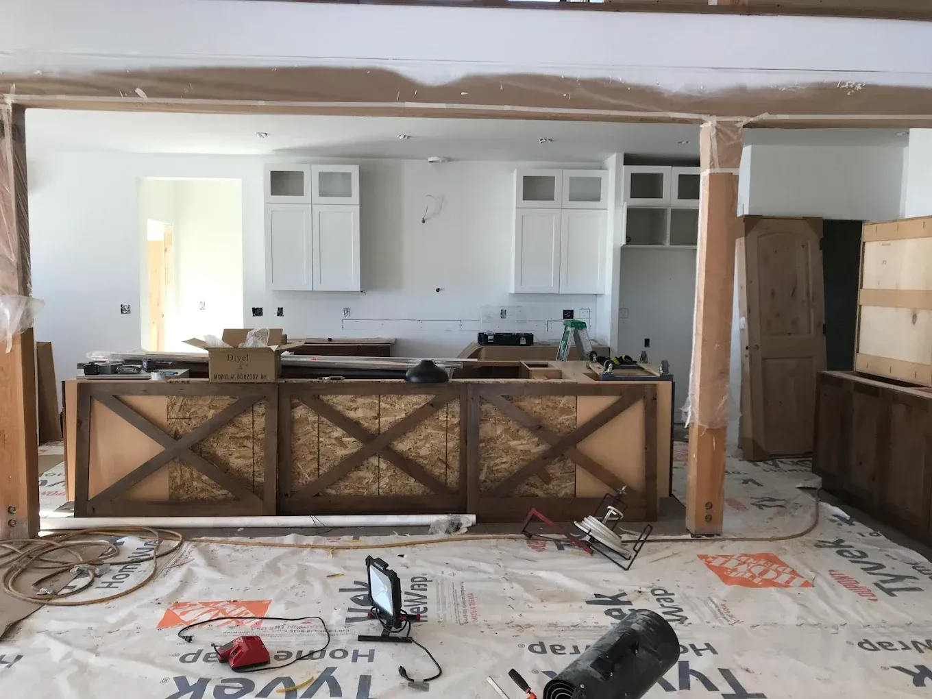 A kitchen renovation in progress featuring a long island with a rustic X-pattern design, white cabinets, and floor covers.