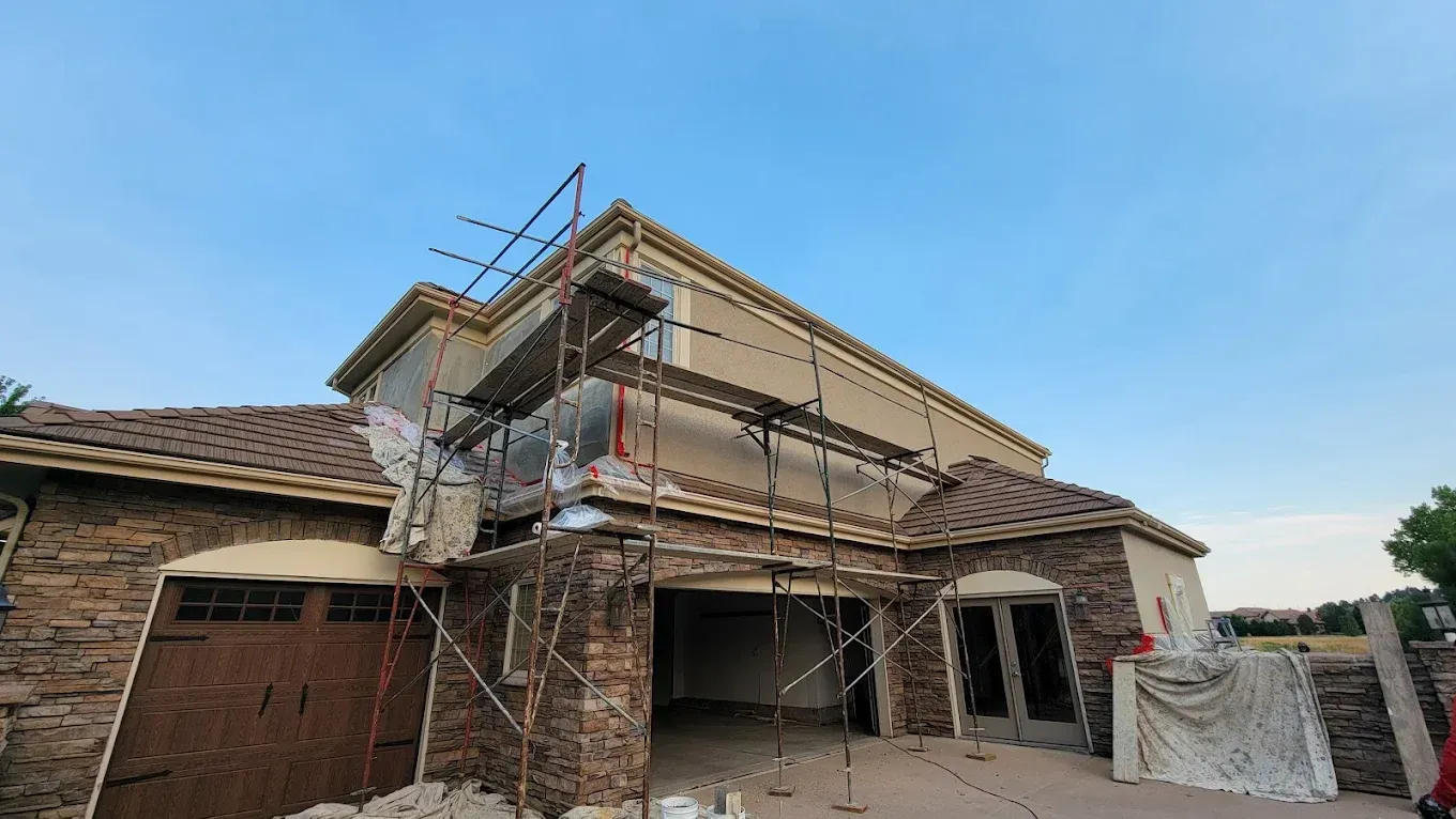 A house under exterior renovation with scaffolding set up against a tan and stone-façade wall.