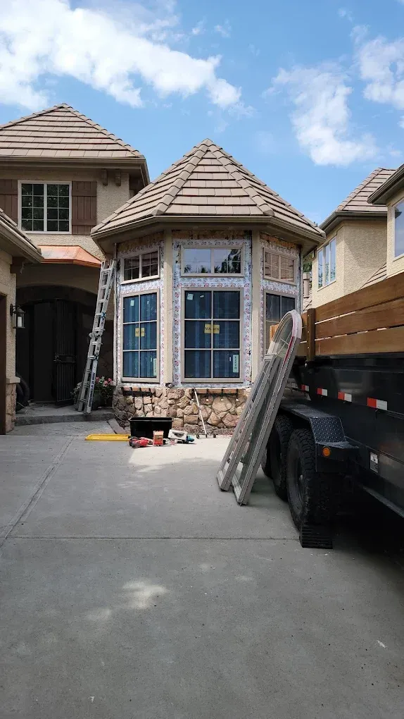 An orange Lull telehandler lifting a wooden wall frame into place at a construction site under a cloudy sky.