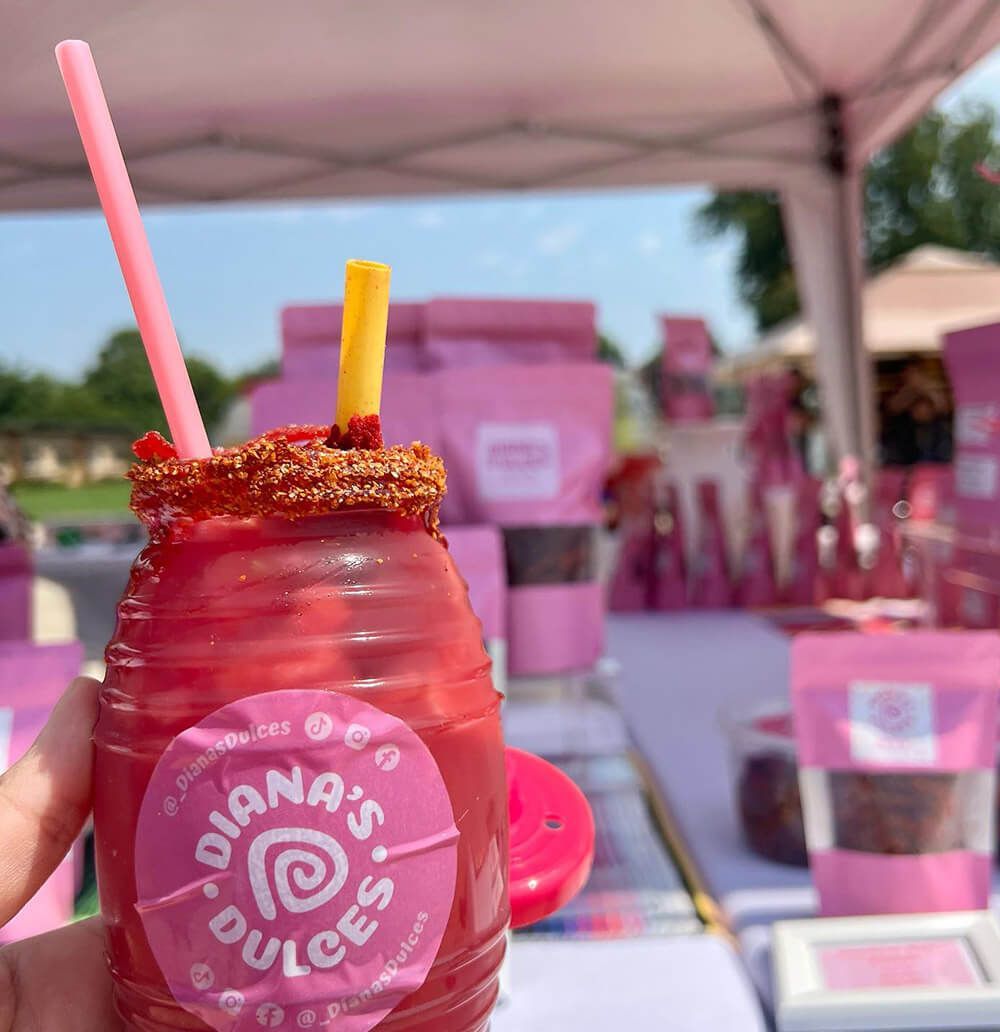 Diana's Dulces agua fresca with chamoy rim and straw, front of ridged cup has a sticker with logo and social handles